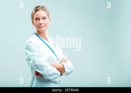 Medico biondo professionista in camice bianco con braccia incrociate. Combina cura con competenza, abilità ed esperienza, rendendola la vostra persona di go-to per Foto Stock