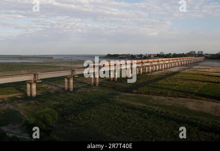 Un treno passeggeri indiano passa sopra un ponte sul fiume Ganges a Prayagraj, India. Le ferrovie svolgono un ruolo importante nel sistema di trasporto pubblico indiano. Foto Stock