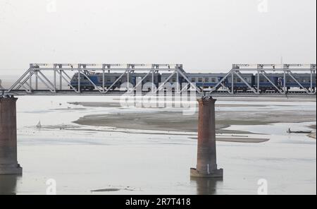 Un treno passeggeri indiano passa sopra un ponte sul fiume Ganges a Prayagraj, India. Le ferrovie svolgono un ruolo importante nel sistema di trasporto pubblico indiano. Foto Stock