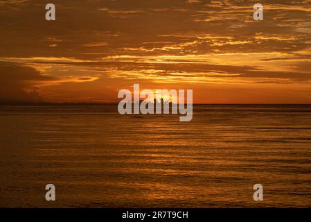 Formazioni di nuvole equatoriali di colore arancione scuro nel Golfo di Tomini al tramonto, viste dalla città costiera e portuale di Ampana nel nord di Sulawesi Foto Stock