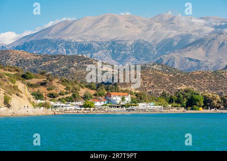 Spiaggia protetta dal vento e baia con lettini e ombrelloni nella popolare località turistica di Agia Galini, nel sud di Creta. Sullo sfondo Foto Stock