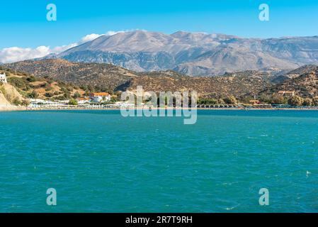 Spiaggia protetta dal vento e baia con lettini e ombrelloni nella popolare località turistica di Agia Galini, nel sud di Creta. Sullo sfondo Foto Stock