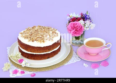 Torta di carote e noci con tazza di tè e fiori estivi su sfondo viola. Piatti deliziosi fatti in casa per il tè pomeridiano o la festa di compleanno. Foto Stock