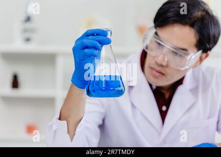 Giovane uomo scienziato asiatico indossando bianco laboratorio uniforme test di ricerca formula medica in laboratorio Foto Stock