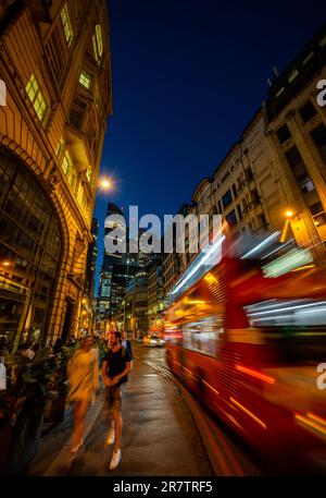 Londra, Regno Unito: Gracechurch Street nella città di Londra di notte. La gente cammina lungo il marciapiede mentre passa un autobus rosso di Londra. Alti edifici dietro. Foto Stock