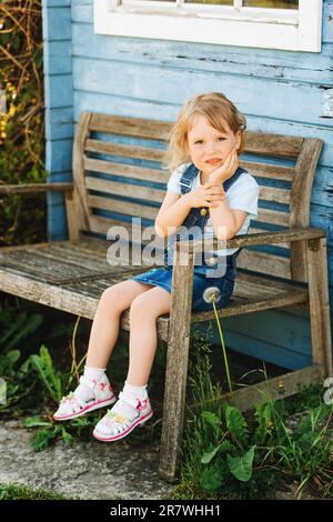 Ritratto all'aperto di carina bambina seduta sulla panchina, felice infanzia in campagna Foto Stock