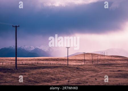 Fotografia di pali telefonici che attraversano una valle contro montagne innevate sull'Isola Sud della Nuova Zelanda Foto Stock
