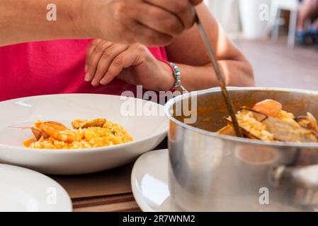 Signora che versa una pentola dalla pentola al piatto di riso con frutti di mare in un ristorante portoghese. Foto Stock