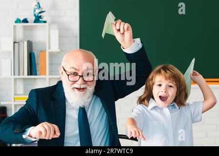 Giornata degli insegnanti. L'insegnante anziano e il giovane studente o il ragazzo della scuola tengono un aereo di carta. Pedagogo e allievo divertirsi Foto Stock