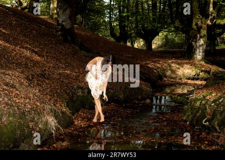 Bellezza a piedi nudi: La donna di brunette passeggerà attraverso una foresta di faggio d'autunno in un abito estivo scorrevole Foto Stock