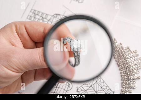 Gioielliere che esamina anello di diamante con lente d'ingrandimento a tavola bianca, primo piano Foto Stock