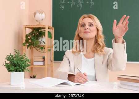 Professore che tiene una lezione vicino al green board alla scrivania in aula Foto Stock
