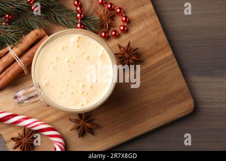 Bicchiere di delizioso egnog e ingredienti su tavolo di legno, piatto. Spazio per il testo Foto Stock