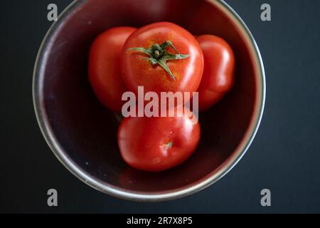 Pomodori in una ciotola di metallo su uno sfondo nero Foto Stock