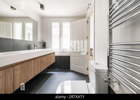 Bagno di design recentemente installato con alto armadio in legno con cassetti allungati, due lavandini monopezzo in porcellana bianca e rubinetti in acciaio inox e ch Foto Stock