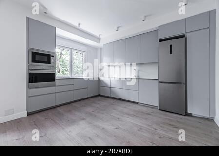 Ampia cucina ristrutturata di recente con armadi grigi, pavimenti in legno chiaro e elettrodomestici in acciaio inossidabile Foto Stock