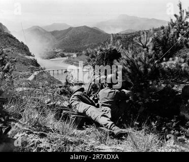 Soldati AMERICANI che presergono una mitragliatrice pesante che domina una valle con un ponte danneggiato durante la guerra di Corea. Foto Stock