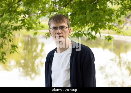 Ritratto di Tall Fit Blond 40 Yo male in occhiali da vista, sorridente guardando la fotocamera, Green Tree e Lake sullo sfondo. Piano orizzontale Foto Stock