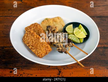 Tempe e Sate Ayam, tempeh e satay di pollo, con lime di kaffir affettate su piatto bianco Foto Stock