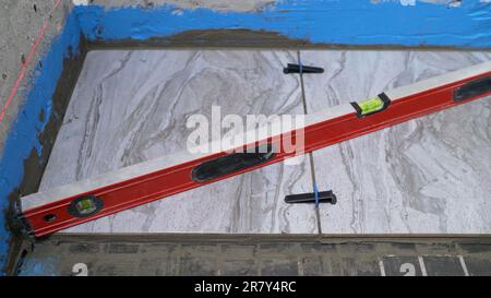 Un tecnico edile sta lavorando, livellando le piastrelle sul pavimento. La piastrella è decorata con bellissime piastrelle sul pavimento del bagno. Posa di piastrelle per pavimenti Foto Stock