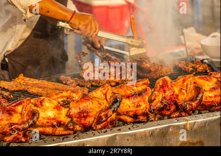 Venditore ambulante in una stalla all'aperto di pollo alla griglia usando un pennello per marinare la carne. Kandal Market, Phnom Penh, Cambogia. © Kraig Lieb Foto Stock