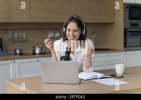Il portacialde femmina si siede al tavolo della cucina parlando nel microfono Foto Stock