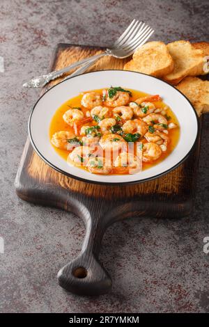 Aglio Spagnolo gamberi Gambas al Ajillo primo piano sul piatto servito con toast sulla tavola di legno. Verticale Foto Stock