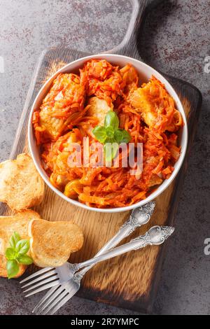 Pesce di nasello brasato con pomodoro, carota, cipolla primo piano sul piatto del legno. Vista verticale dall'alto Foto Stock