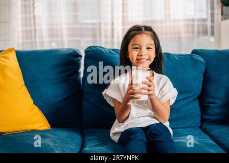 Ritratto sorridente di ragazza carina asiatica che tiene un bicchiere di latte a casa Foto Stock