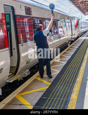 Grantham Train Station – Una direttrice o guardia femminile che spedisce un treno Azuma London North Eastern (LNER) dalla piattaforma Foto Stock