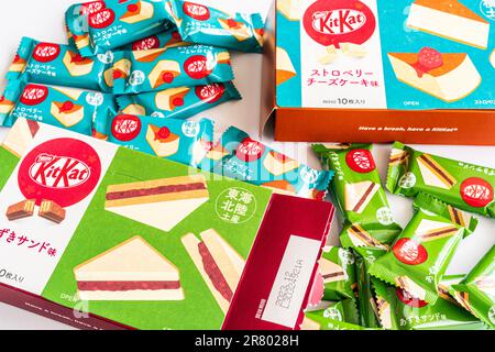 Due confezioni di kitkat giapponesi di fagiolo rosso e fragola con diverse mini-bar avvolti da due dita disposte intorno a loro. Foto Stock