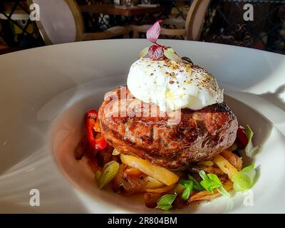 cotoletta di manzo tritata su un cuscino di patate con lattuga, uova in camicia e sugo piccante Foto Stock