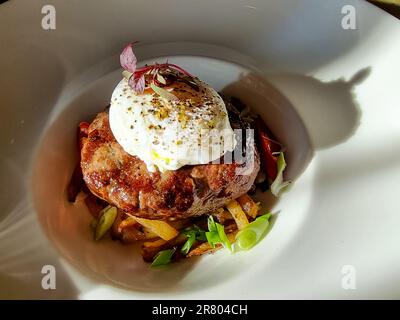 cotoletta di manzo tritata su un cuscino di patate con lattuga, uova in camicia e sugo piccante Foto Stock