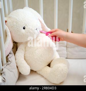 Il bambino sta dimostrando l'igiene dentale alla sua lepre giocattolo mostrandogli come spazzolare i denti con uno spazzolino da denti. Bambino di circa due anni (su Foto Stock