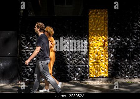 Una donna e un uomo che passa un'entrata nera e dorata di un bar a Hohenzollernring, Colonia, Germania. Eine Frau und ein Mann passieren den schwarz-g Foto Stock