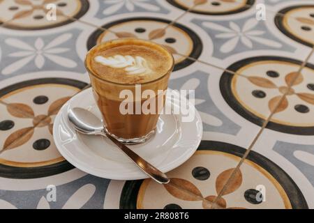 Bicchiere di caffè espresso appena preparato con latte cremoso su vetreria da tavolo a mosaico per cappuccino mocaccino americano con latte di cocco. CA Foto Stock
