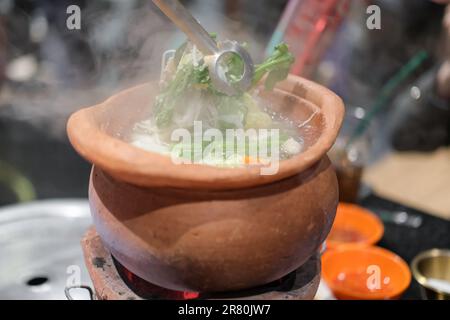 Jim Joom, una pentola calda in stile thailandese del nord-est della Thailandia, contiene maiale, verdure e spaghetti in vetro in una terrina di argilla Foto Stock