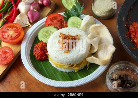 Cucina indonesiana su tavola di legno. Hamburger di riso con pollo piccante, omelette all'uovo, acciughe di pesce, filo interdentale di manzo, croccante di gamberi, pomodoro, cetrioli, sedano, sambal Foto Stock