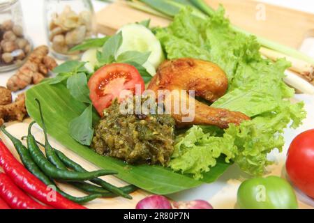 Pollo fritto galangale, sambal, pomodoro, cetriolo, basilico, lattuga. Cucina indonesiana con piatti a foglia di banana. Arte culinaria, fotografia e ingredienti spezie Foto Stock