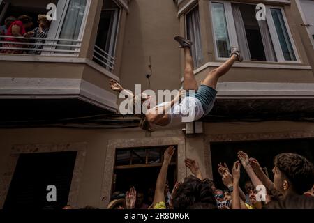 Ciutadella, Spagna. 18th giugno, 2023. Una ragazza viene gettato in aria mentre un giovane uomo rivestito in una pelle di pecora, l''Homo des Be' (uomo di pecora), portando un ariete vivo intorno alle sue spalle la Domenica prima che il festival di San Giovanni di Ciutadella visita la casa di un 'caixer' (cavaliere) Credit: Matthias Oesterle/Alamy Live News Foto Stock