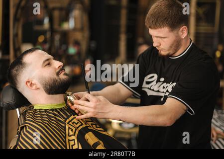 Primo piano dei rivestimenti professionali del barbiere per la barba del cliente. Bell'uomo barbuto in barbiere Foto Stock