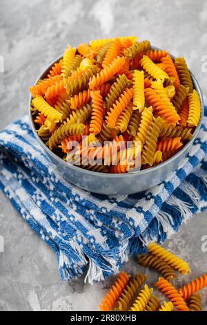 Fusilli crudi su calcestruzzo. Pasta cruda italiana colorata su un tovagliolo di lino. Cucina italiana Foto Stock