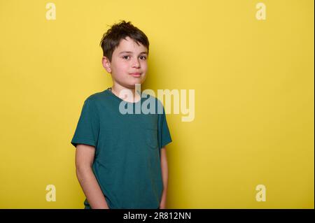 Bel ragazzo ragazzo maschile sorride guardando la macchina fotografica, in piedi su sfondo giallo isolato con le mani in tasca Foto Stock