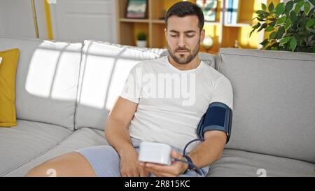 Giovane uomo ispanico che misura l'impulso usando il tensiometro a casa Foto Stock