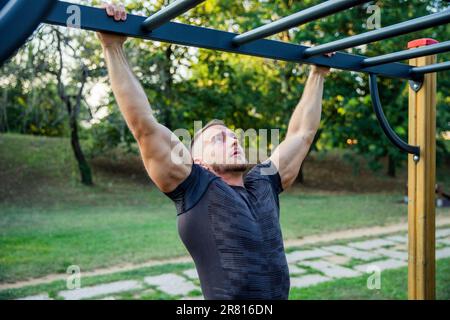 Un uomo in forma si allena in un parco all'aperto con bar, allenamento all'aperto Foto Stock