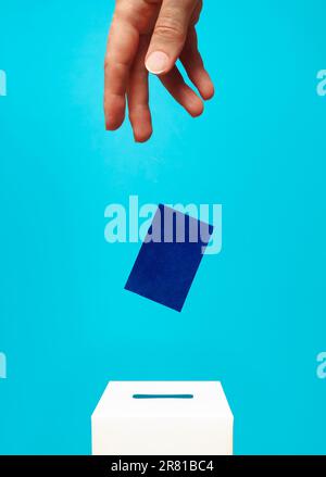 concetto di elezione - la mano di una donna mette una carta blu in una casella di voto bianca con una fessura, lo sfondo è blu, levitazione Foto Stock