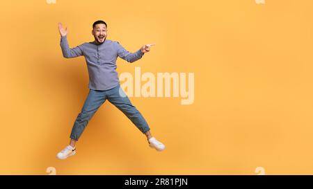 Giovane uomo asiatico positivo che mostra lo spazio di copia mentre salti in aria Foto Stock