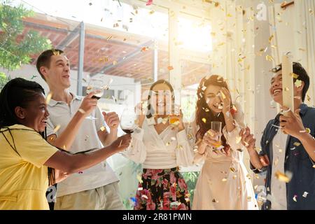 Gruppo di amici entusiasti che ballano sotto i coriandoli durante la festa di compleanno di casa Foto Stock