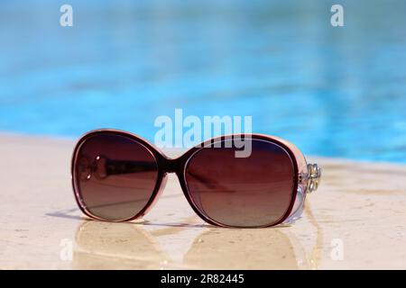 Occhiali da sole sul bordo della piscina con acqua blu. Vacanza al sole sulla spiaggia Foto Stock