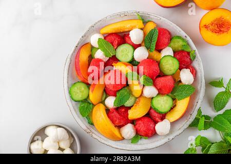 Insalata estiva di frutta a base di frutta fresca, mozzarella, cetrioli e menta su tavola bianca. vista dall'alto Foto Stock